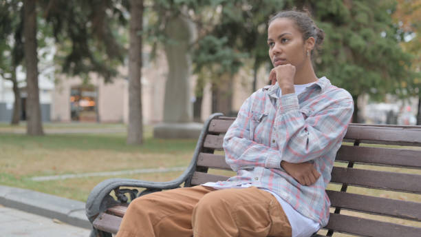 istock Pensive African Woman Thinking while Sitting Outdoor on Bench 1440381764