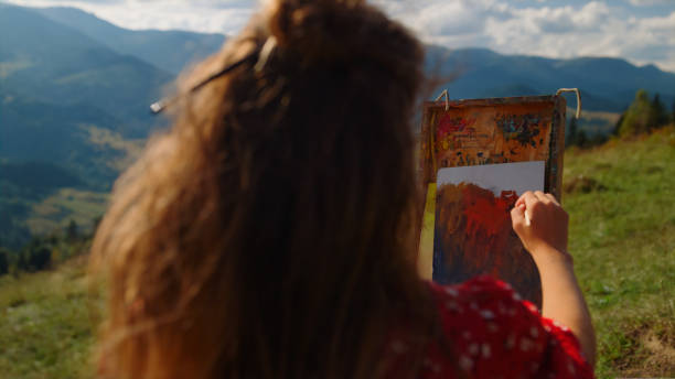 istock Back view woman painter drawing on easel beautiful mountains landscape close up. 1440385864