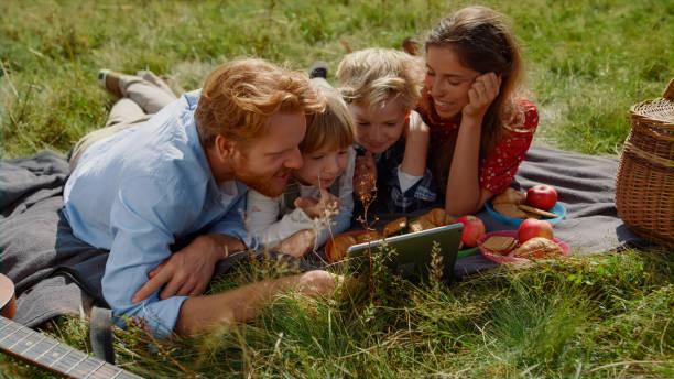 istock Family watching tablet computer on picnic lying green grass. Summer vacation. 1440386521