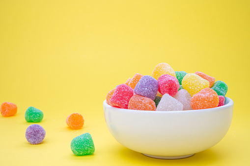 Colorful gum drops in a bowl  on a yellow background with a scattering of gum drops