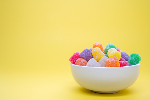 Colorful gum drops in a bowl on a yellow background
