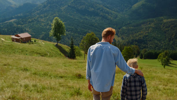 istock Back view father son walking on green hill. Parent with boy going down slope. 1440393208