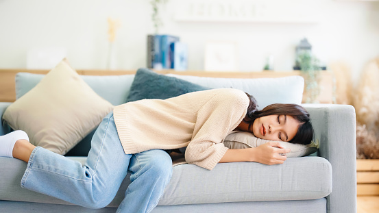 Asian woman resting at home on couch, feeling exhausted after work, lacking energy, or overworked, too tired, and lacking motivation