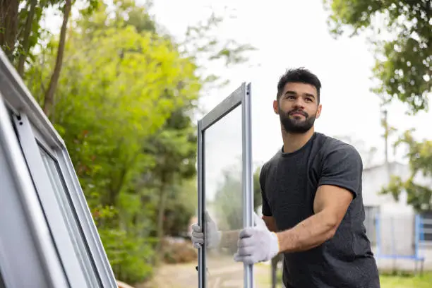 Handsome Latin American construction worker carrying a panel of a sliding door while building a house