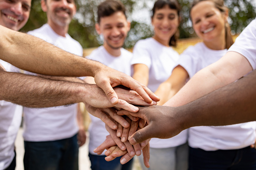 Happy group of volunteers in a circle with their hands together in the middle outdoors - charity work concepts