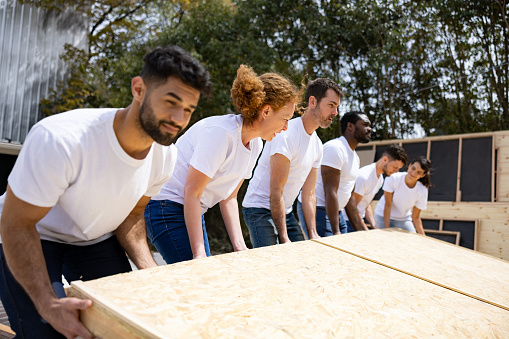 Group of Latin American volunteers lifting a panel while building a manufactured house - construction concepts