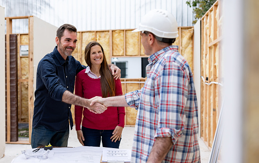 Happy couple greeting the architect building their house with handshake at a construction site