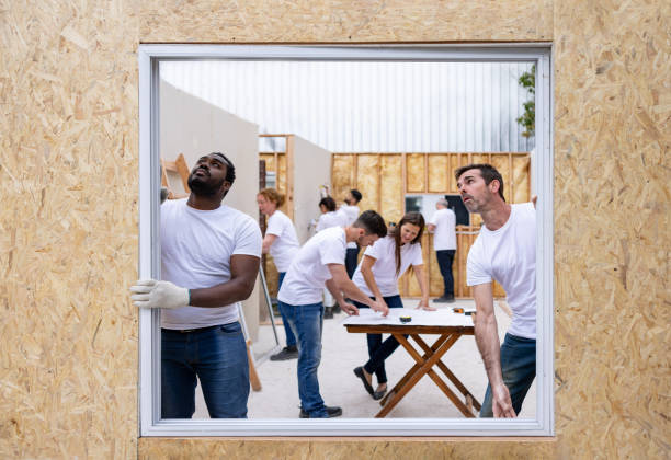 волонтеры устанавливают окно при строительстве дома - housing development organized group house real estate стоковые фото и изображения