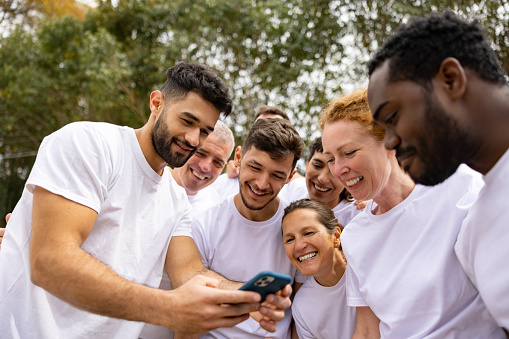 Happy group of Latin American volunteers looking at a post on social madia while smiling outdoors