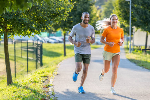 jeune couple souriant faisant du jogging dans le parc de la ville ensemble - course à pied photos et images de collection