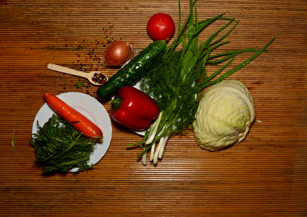 fresh vegetables of different types on a dark background for salad grass rakula tomatoes peppers wooden spoon onion cabbage carrots and other vegetables tomato, sweet pepper, greens, cucumber, light wooden spoon, onion, arugula herb with meat taste