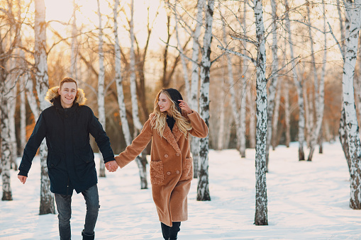 Loving young couple walking playing and having fun in winter forest park.