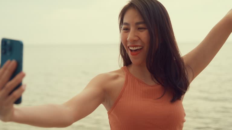 Young Asian woman using smartphone taking a selfie on tropical beach.