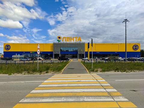 Noyabrsk, Russia - July 1, 2022: View across the road of the large yellow and blue building of the Lenta store on a summer day.