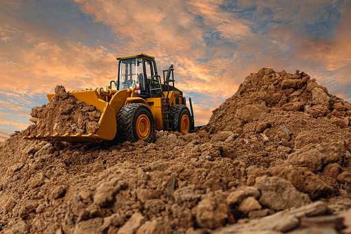 Wheel loader are digging the soil in the construction site on the  sky background after sunset