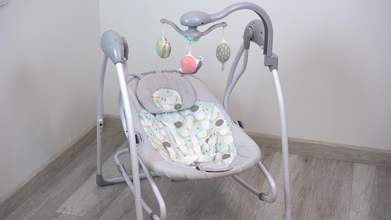 An empty swing-cradle swings in the room. Children's automatic swing for an infant. 4k