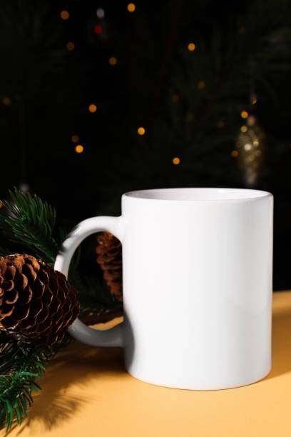istock White ceramic mug close-up on a beige background with fir branches and defocus lights. Mockup with cup for copy space and logo. 1440433602