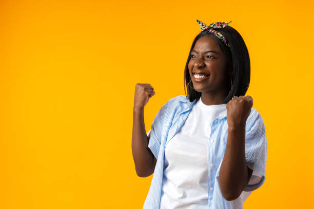 Portrait of a cheerful african woman with hands raised on yellow background stock photo