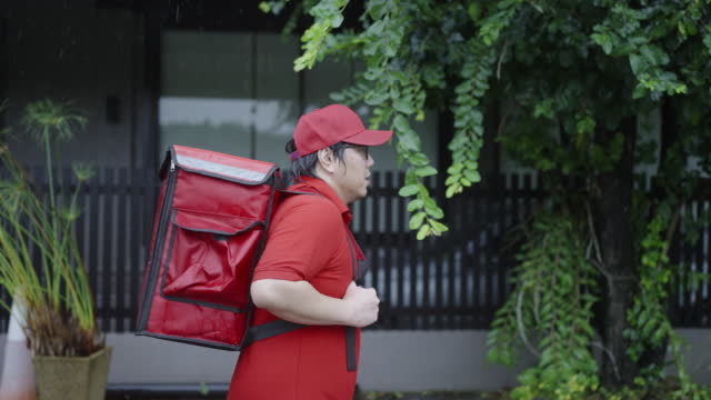 Asian delivery guy walking on the sidewalk carrying food delivery box on his shoulders feeling tired.