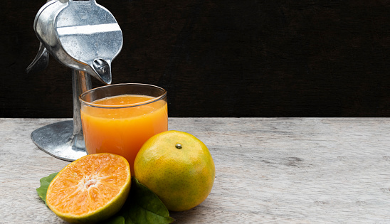 Orange juice in glass and fresh citrus around with Juicer hand press squeezer fruit on wood table. Copy space