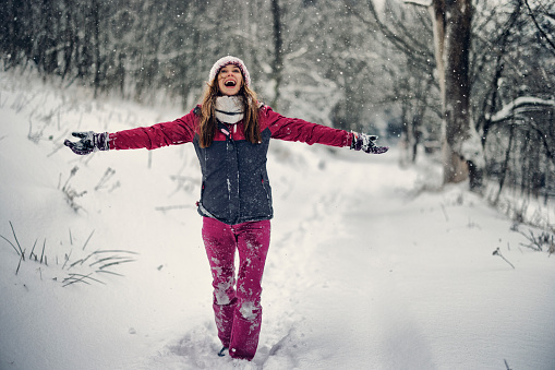 Happy young happy woman with raised hands and enjoys the snow in mountains.