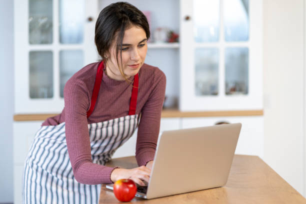 istock Young female baker sitting on kitchen counter typing on laptop 1440440840