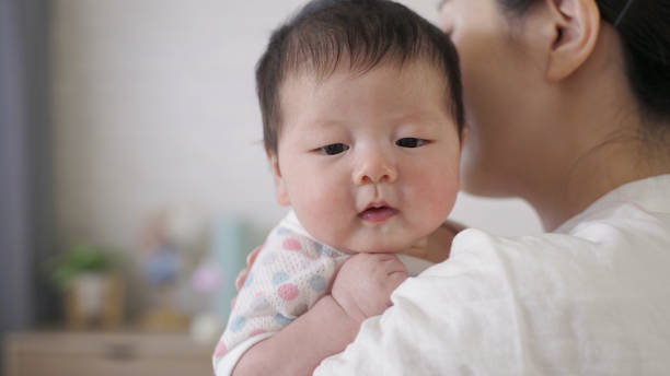 plan rapproché l’adorable petite fille dans les bras de sa mère est un peu contrariée alors qu’on rote et tapote le dos à la maison. - pat on back photos et images de collection