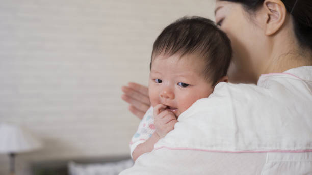istock selective focus cute newborn infant is looking at camera innocently as her mommy is helping her burp at blurred background bright nursery room. 1440442206