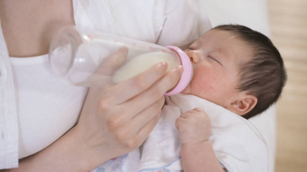 istock young infant is drinking milk with eyes close while its parent is using fingers to touch the bottle lightly in the bedchamber with cropped shot. 1440442296