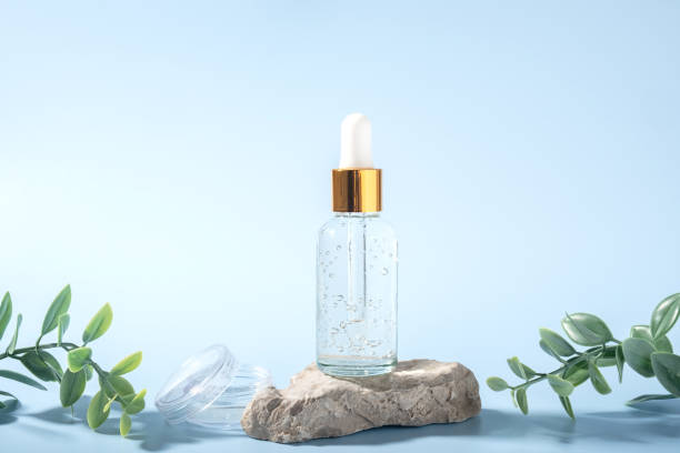istock Transparent glass cosmetic bottle on stone on light blue background with green branches. Natural organic spa anti age cosmetic and new naturalism concept. Copy space. 1440443575