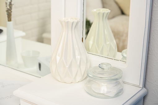 A glamorous dressing table. A table for the lady. White fashion box, space for text. On the table is a white vase and a glass jar. You can see the mirror.