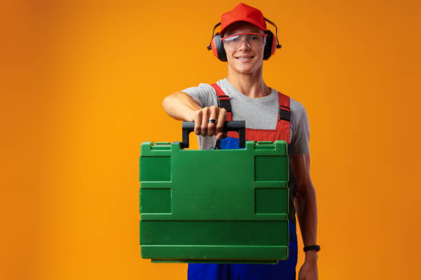 Portrait of young foreman worker with toolbox over yellow background in studio