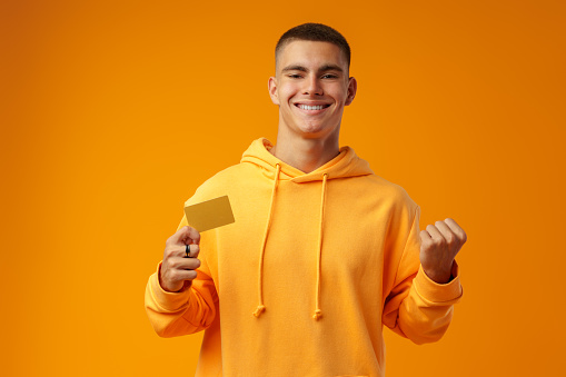 Young handsome man over yellow background holding a credit card in studio