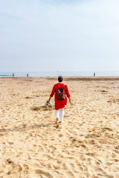 istock Female tourist walking barefoot along seashore 1440448653
