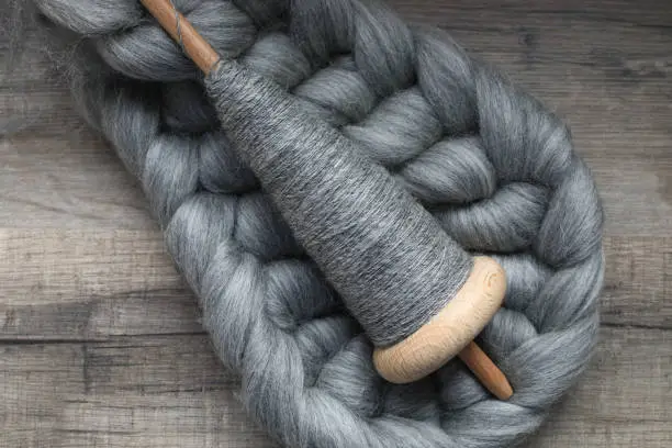 Handspinning hobby displaying a handspun yarn on a wooden handspindle with natural sheep wool.
