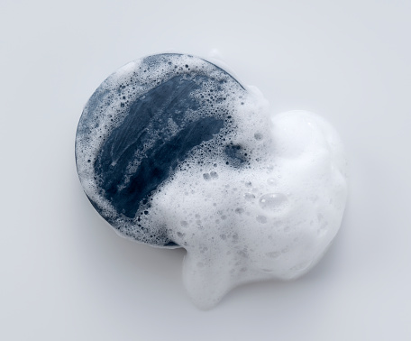 Solid soap with foam placed on white background. Viewed from directly above.