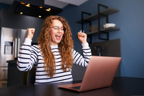 Female rejoice, celebrate bank loan acception, big lottery win, auction victory, profitable bet on crypto stock market. Woman checks e-mail, news about success on laptop, happily throws up papers. stock photo