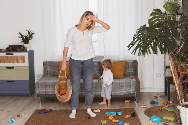 young woman, housewife puts toys in the basket with her little son at home stock photo
