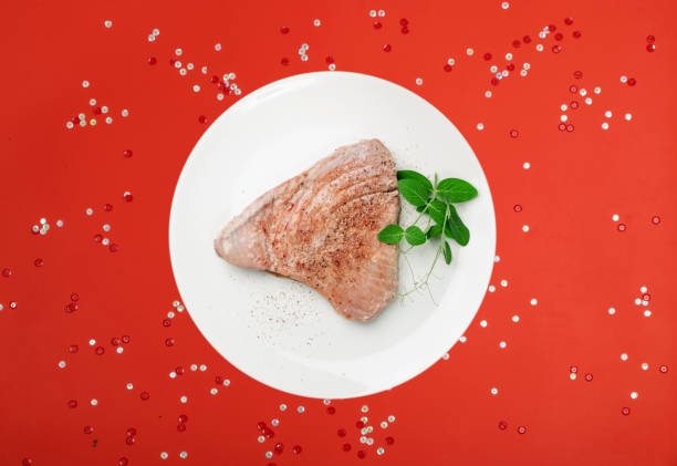 Roasted tuna steak on red christmas background. Red sea fish fillet, medium roast tuna filet, tuna steak top view