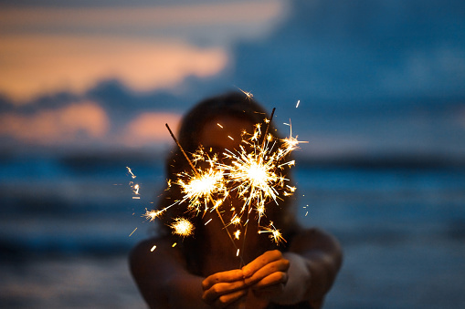 Young woman with sparklers on the beach at sunset