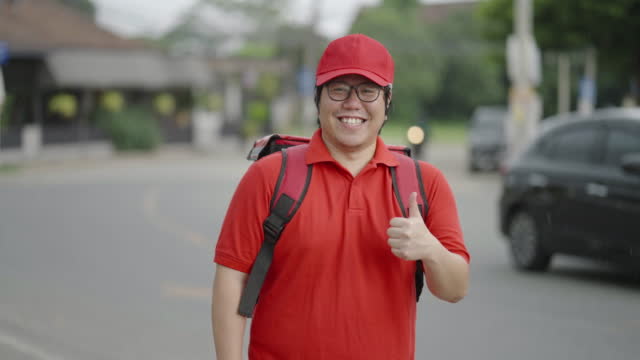 Rear view of food delivery man standing then turning around to look at camera and giving a thumbs up with cheerful face.