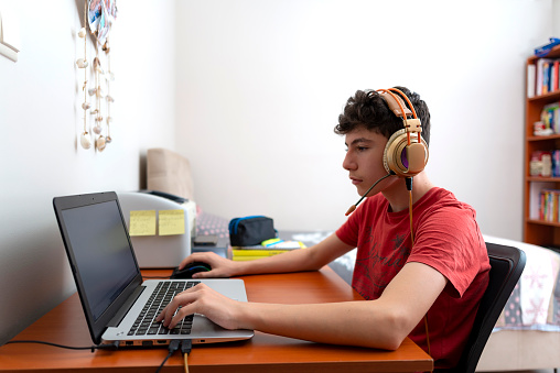 Teenage boy is studying via pc. The boy doing his homework on the computer in his room is holding a live conference.