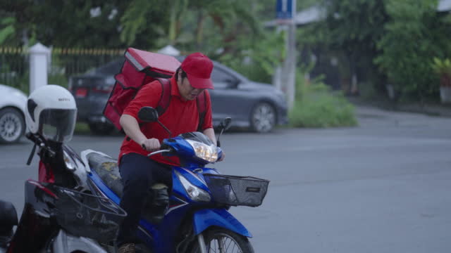 Delivery man riding and parking motorcycle before walking to deliver customer order in a residential area.