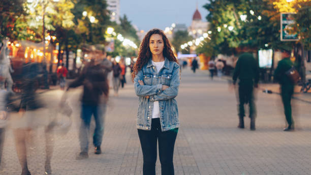 portrait d’une jeune femme élégante fatiguée de la hâte habituelle debout dans la rue parmi des gens sifflants et regardant la caméra. concept de temps, de jeunesse et de société. - sea of tranquility photos et images de collection