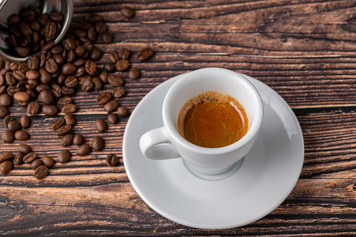 Coffee in a red coffee cup with raw coffee beans around it on a wooden table.