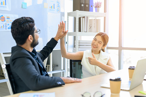 businessman and businesswoman giving hi five or touching hands and thumb up at modern office. business union and success concept