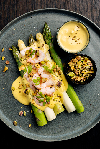 Overhead view of green and white asparagus served with prawns and a hollandaise sauce and sprinkled with pistachios.