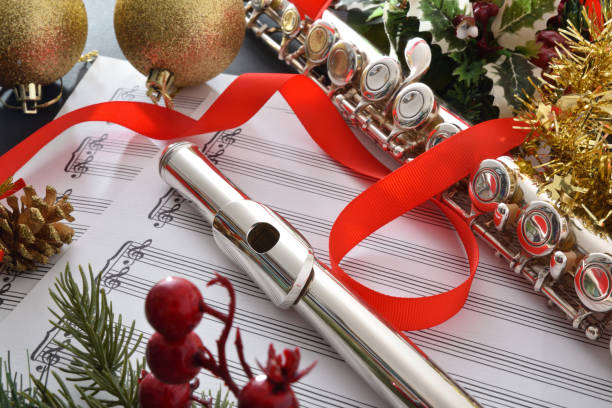 Detail of flute on music sheet ribbon and Christmas decoration Transverse flute on music sheet with Christmas decoration on black table close up. Elevated view. brass horn stock pictures, royalty-free photos & images