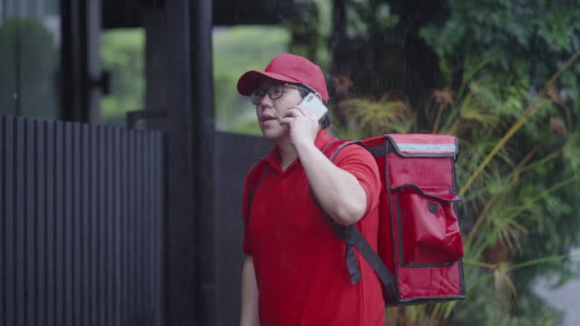 Wet food delivery guy calling customer using smart phone to inform customer of his arrival in front of customer's house.