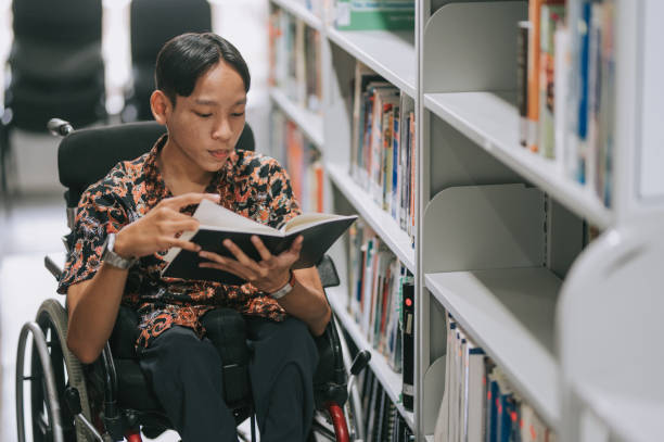 ragazzo adolescente asiatico con disabilità in sedia a rotelle libro di lettura in biblioteca - library education teenager student foto e immagini stock